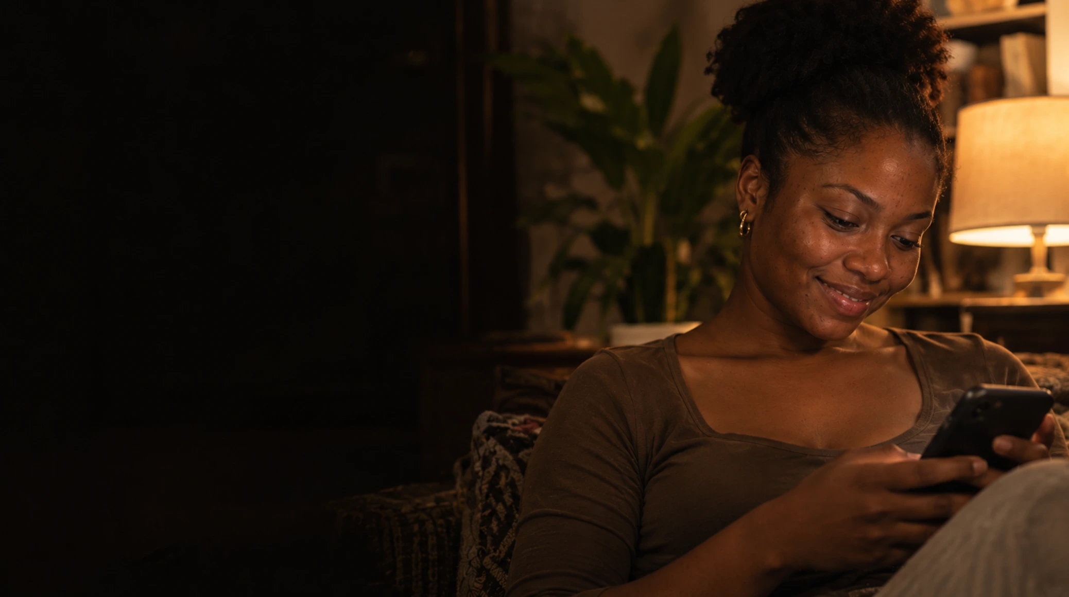A woman smiling at her phone while relaxing at home in the evening